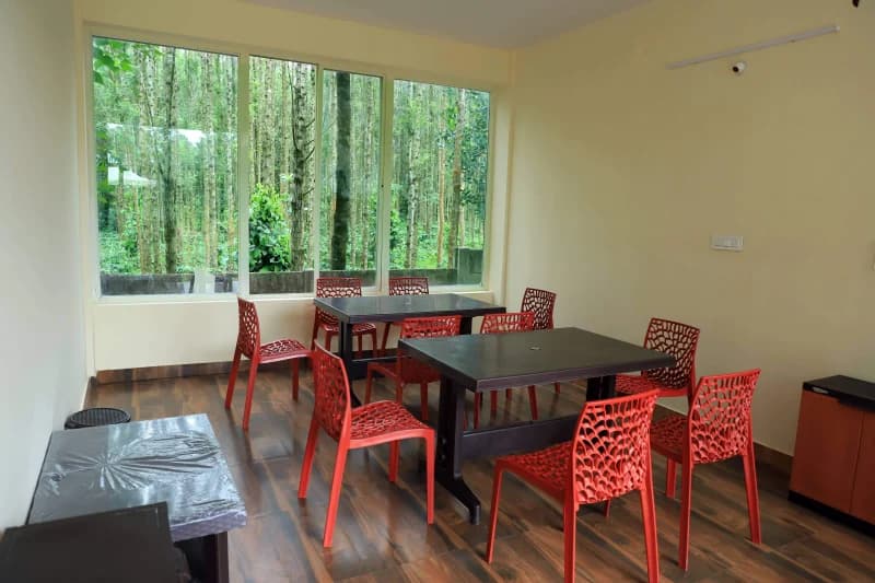 Red chairs and a shared table overlooking trees at Trippr Chikkamagaluru