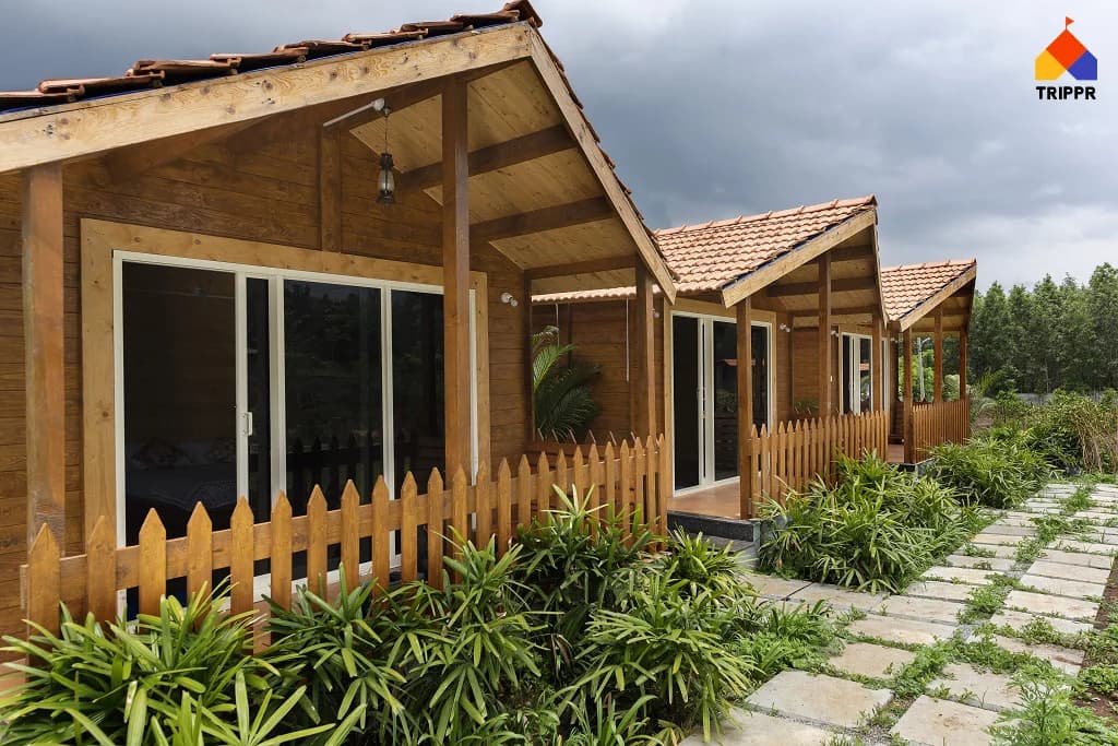 Timber cottages beside a planted stone walkway at Trippr Chikkamagaluru