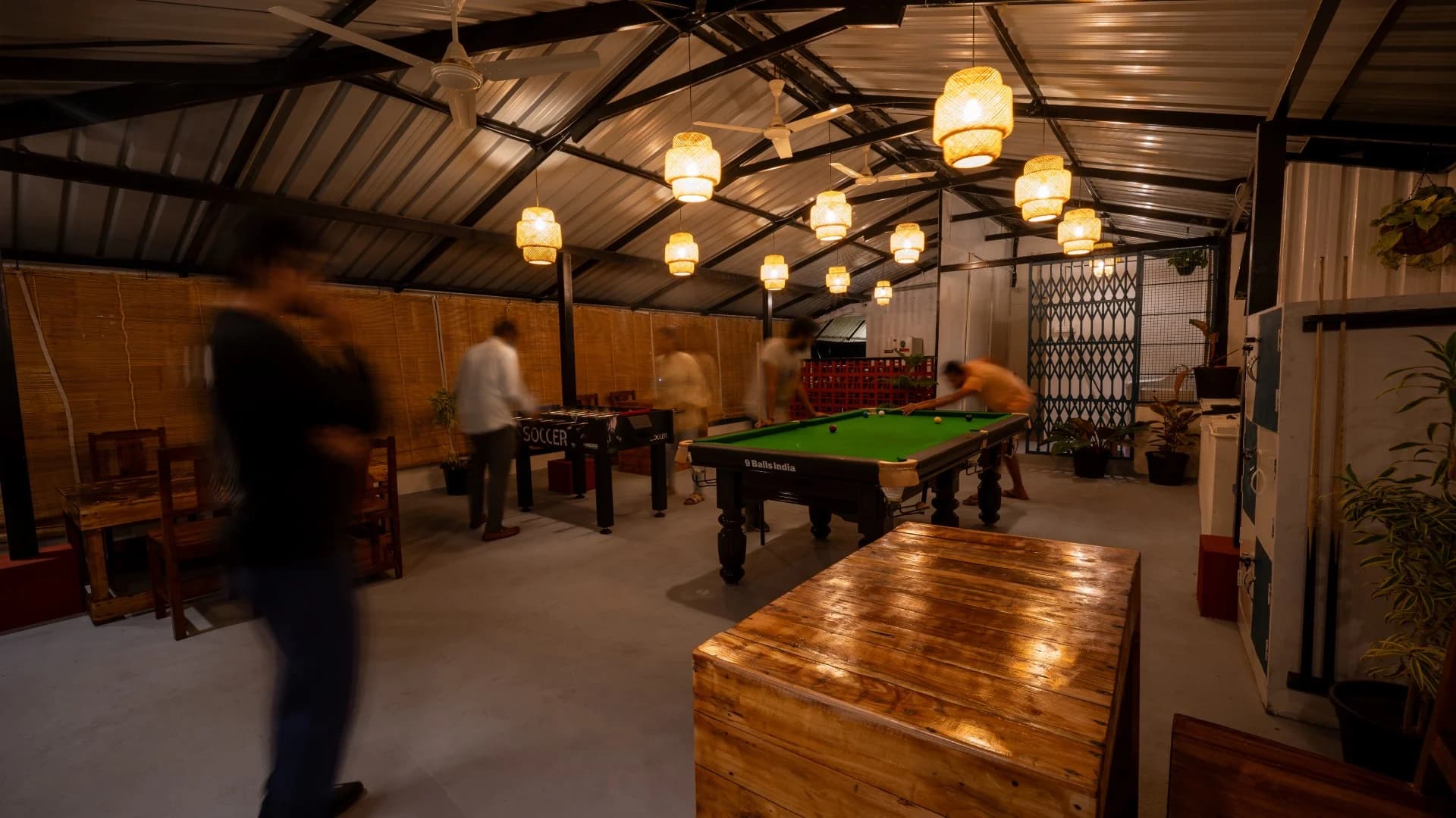 Rooftop common area with a pool table and hanging lights at Trippr Mysuru